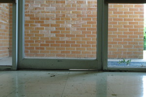 Image of a metal framed exterior glass door with a gap between the door fame and the floor, allowing sunlight through
