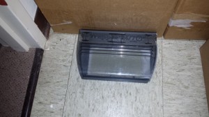 Image of a closed trapping device placed on the indoor floor adjacent to a wooden cabinet
