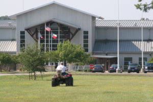 Man driving a fire ant bait broadcast spreader at a school